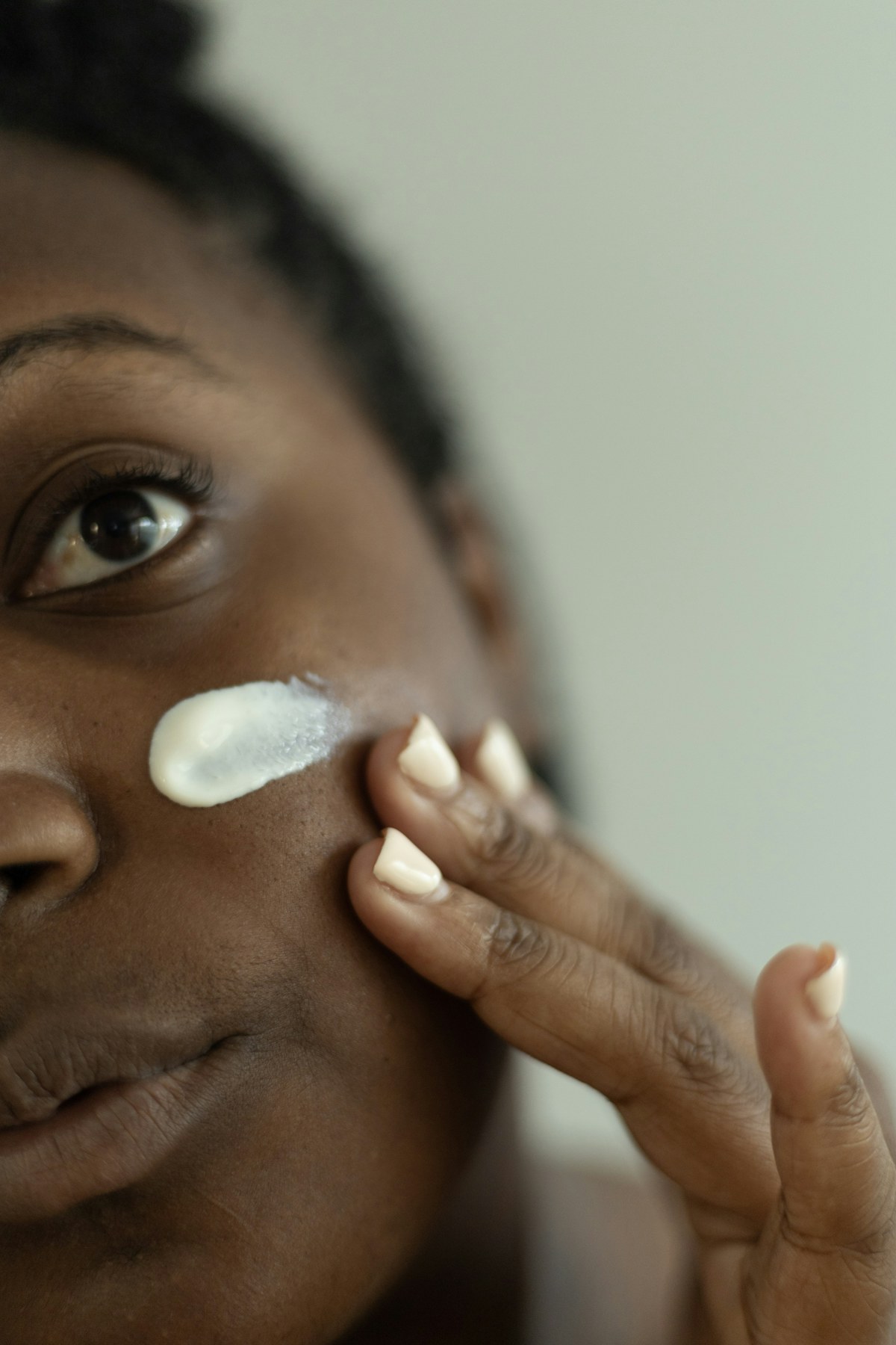 Fotografia de uma mulher aplicando creme no rosto, ilustrando cuidados cotidianos com a pele.