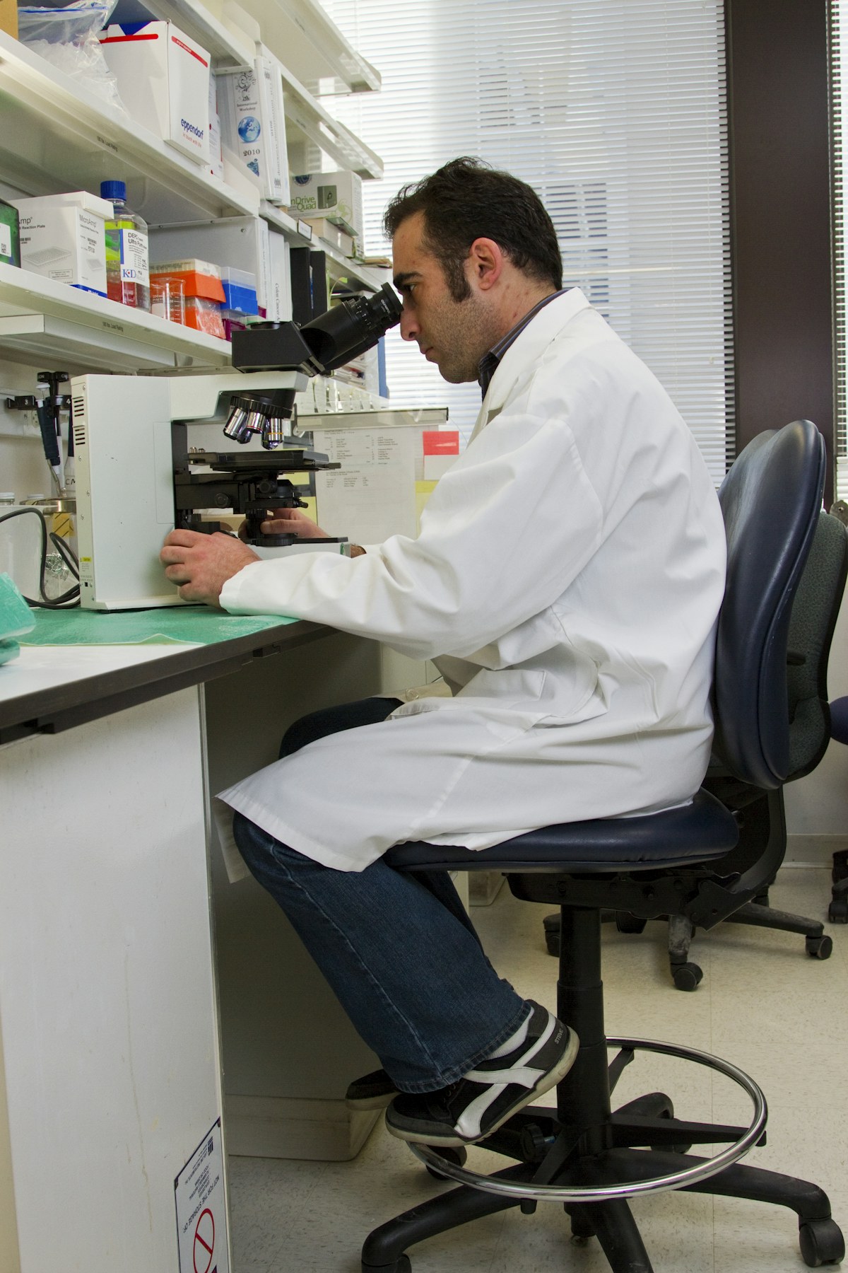 Fotografia de pesquisador usando microscópio em laboratório, ilustrando pesquisa científica.